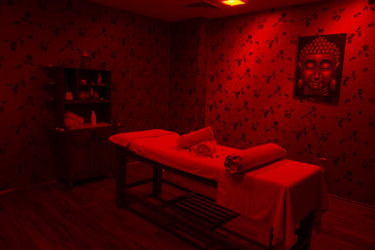 Serene massage room with red lighting featuring a Buddha portrait, ideal for relaxation and self-care.